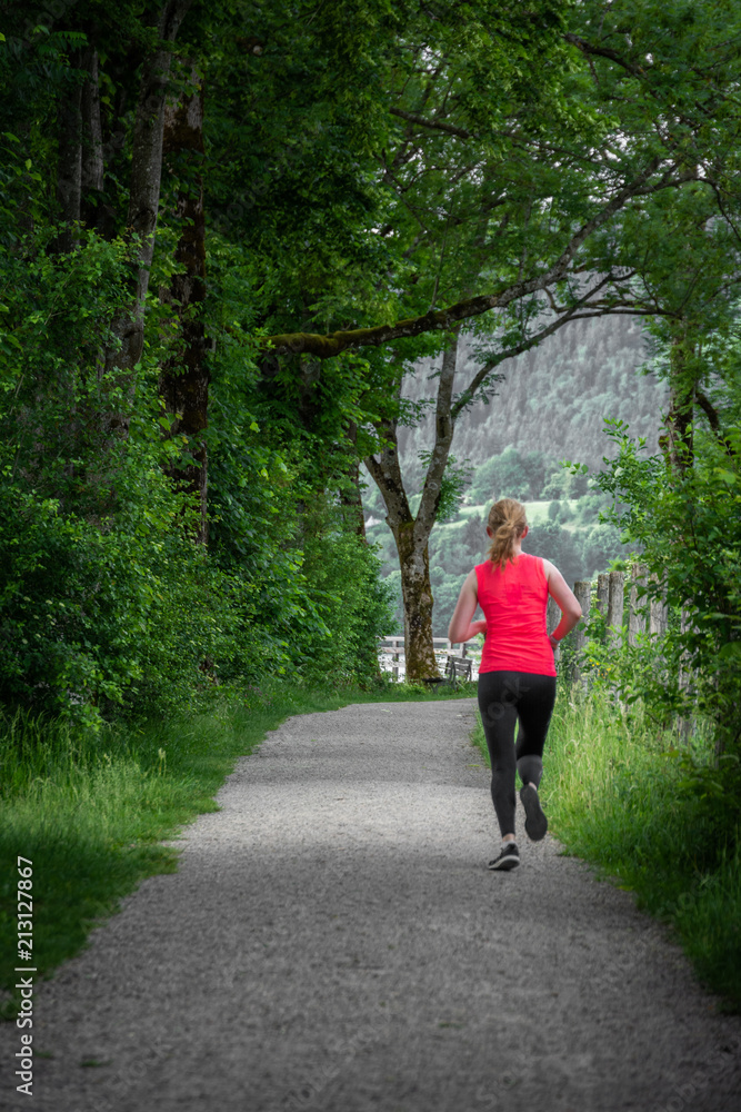 Young woman running along path surrounded by trees Young woman running along path surrounded by trees