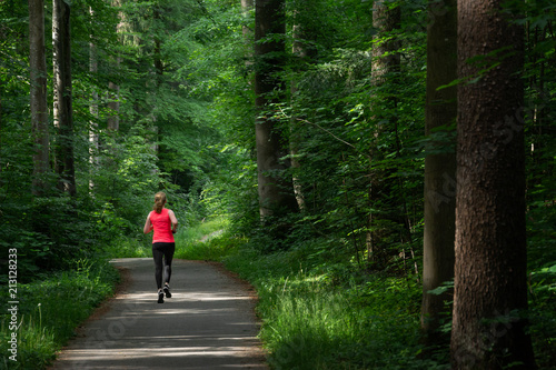 Young woman running along path through green forest.