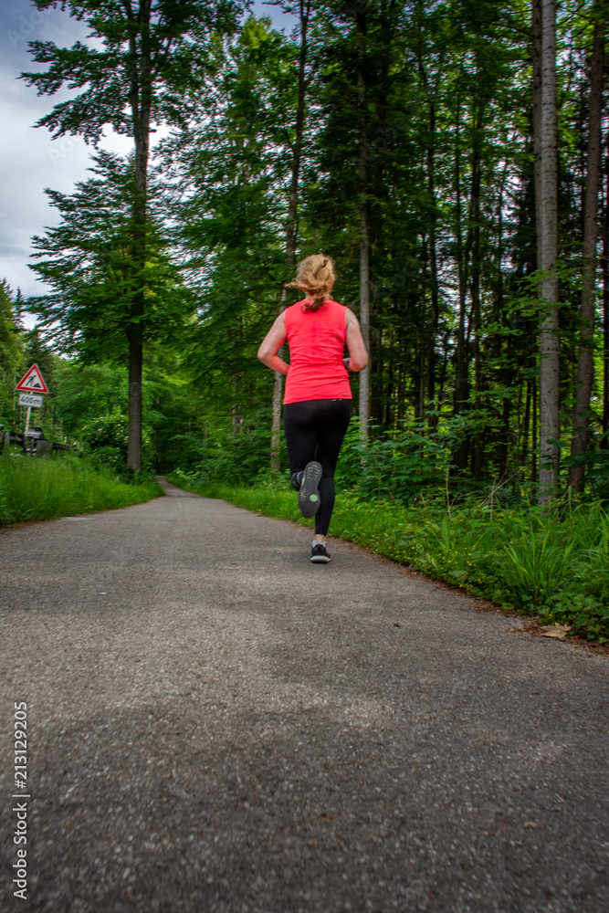 Young woman running along curved path through green forest. Young woman running along curved path through green forest.