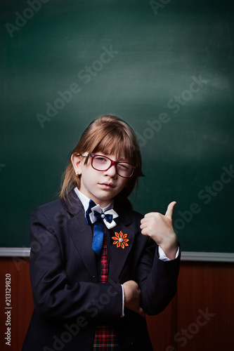 back to school. love to learning. Thumb up. The girl in uniform and glasses smiles, gestures to the side, against the background of the school board.