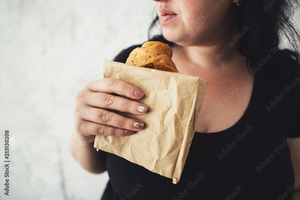 Unhealthy fattening food,high-calorie snack, eating on the go, take-out meals. Overweight woman eating croissant, free space for text design Unhealthy fattening food,high-calorie snack, eating on the go, take-out meals. Overweight woman eating croissant, free space for text design
