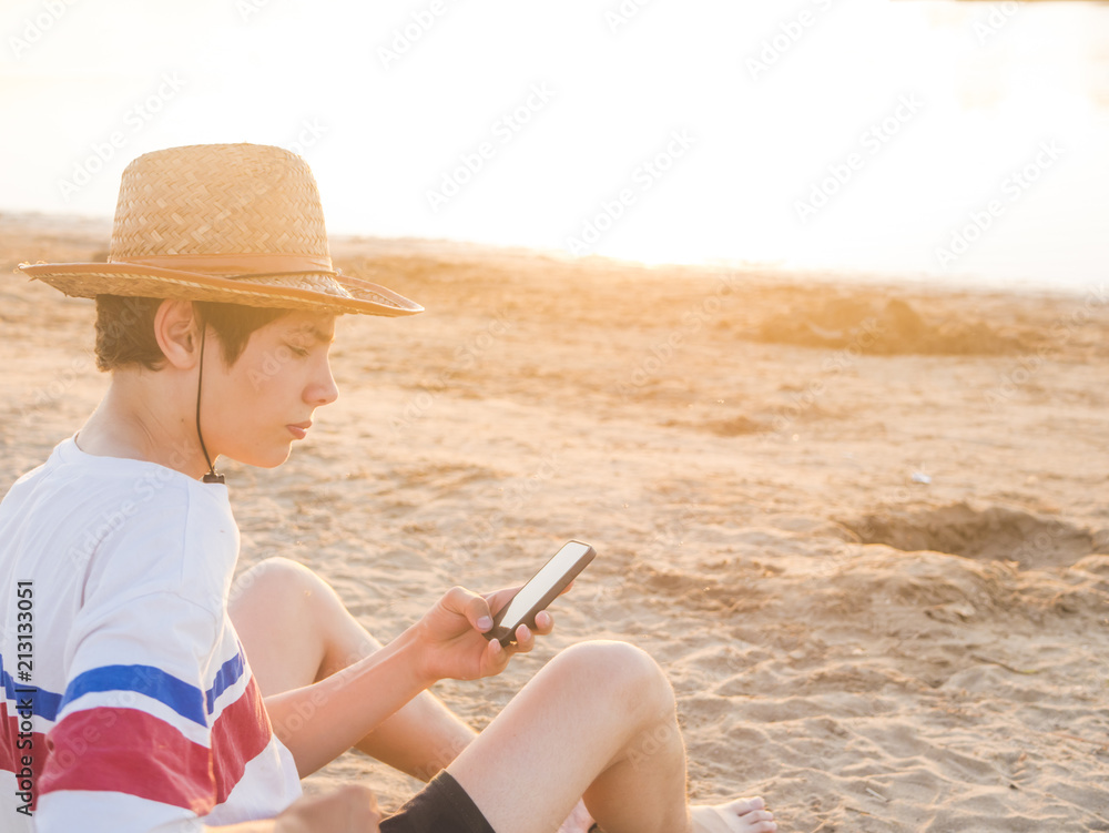 lifestyle photo of young man portrait in summer hat and casual clothes with phone on a sandy sea beach