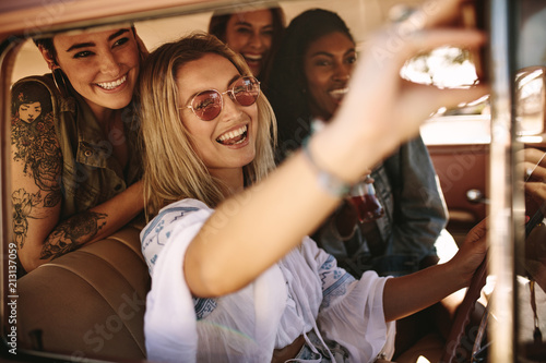 Woman driving a car and making selfie with friends