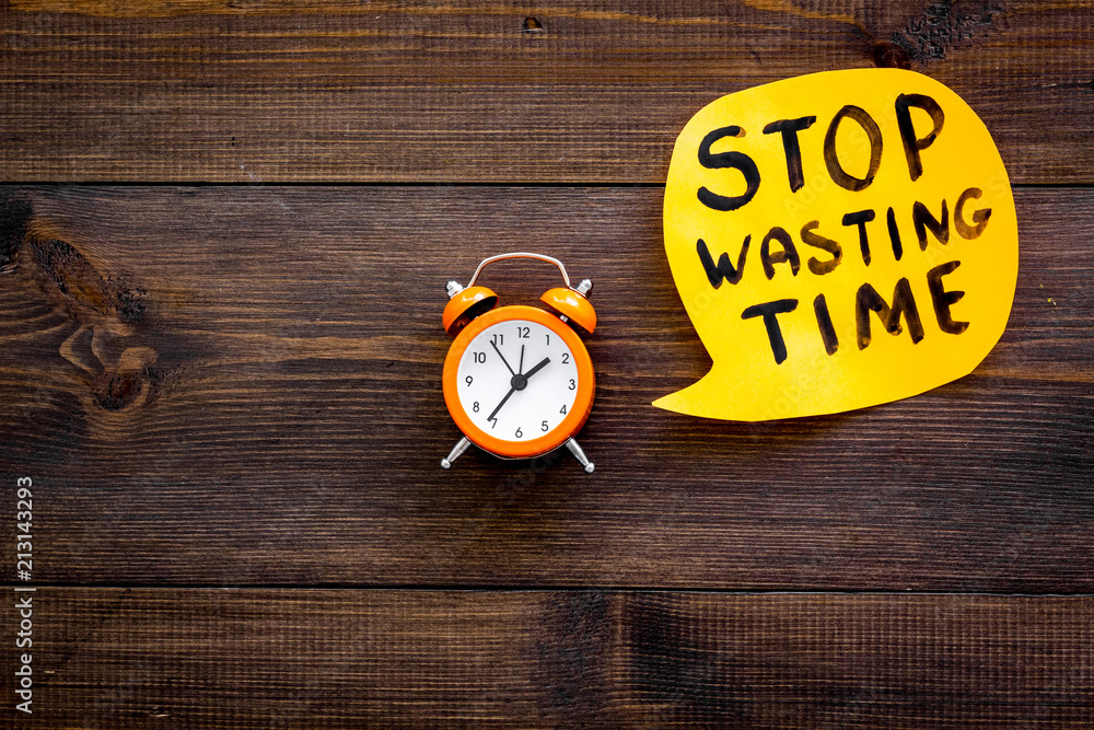 Stop wasting time hand letterng in cloud near alarm clock on dark wooden background top view copy space. Business concept, motivation Stop wasting time hand letterng in cloud near alarm clock on dark wooden background top view copy space. Business concept, motivation