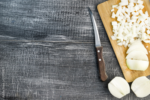 Sliced onions on a board with an aged knife on a dark wood background with copy space. Image of onion cutting.