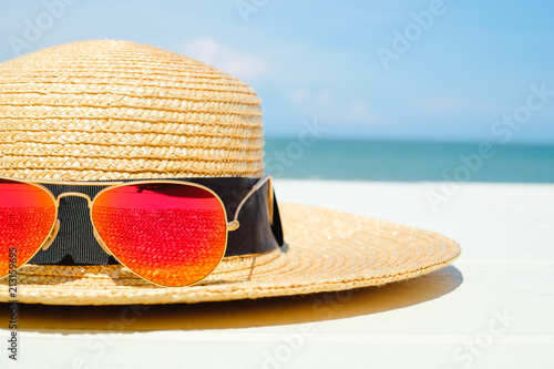 Colorful orange sunglasses on bamboo hat on white wooden table with sea and blue sky cloud background with copy space.summer season.