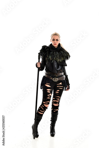 full length portrait of blonde girl wearing black gothic outfit, holding a staff. standing pose, isolated on white studio background.