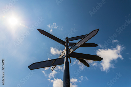 Black metal signpost with arrows in different directions, blue sky in the background.