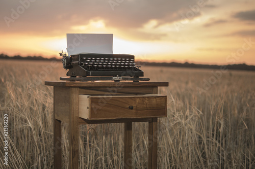 typewriter on a walnut bedside table in a wheat field at sunset photo