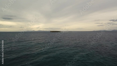 Flying over the sea on a cloudy day. Small island on the horizon. photo