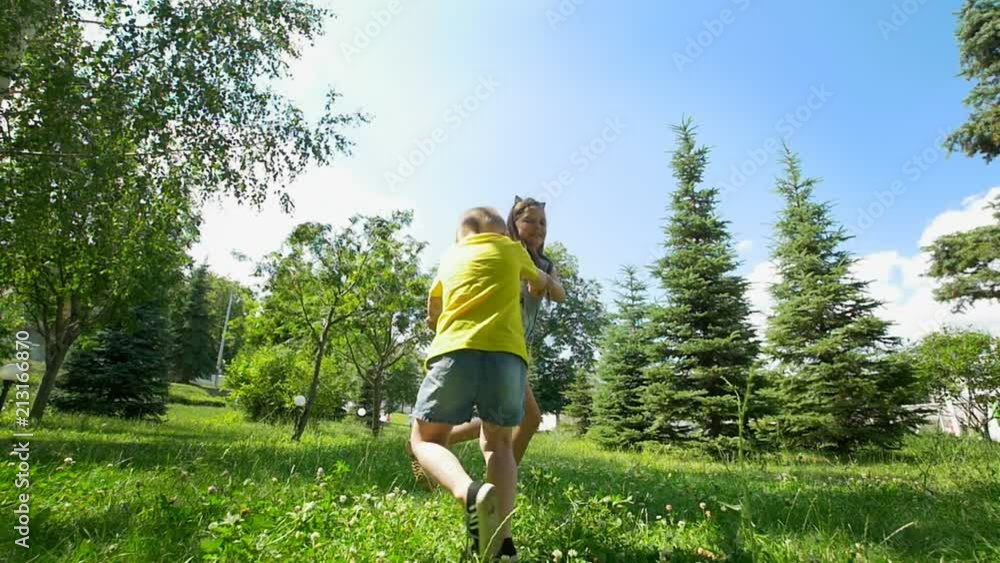 Cute little boy runs away from his happy sister through the spruce trees at sunny day Cute little boy runs away from his happy sister through the spruce trees at sunny day
