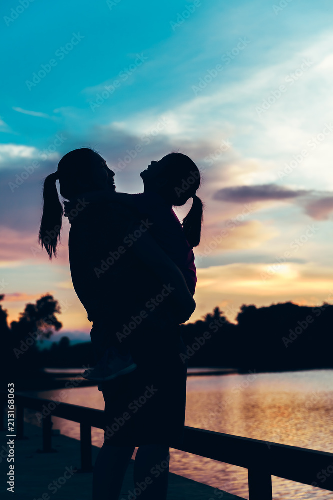 Silhouette of mother and her daughter enjoying view at riverside.