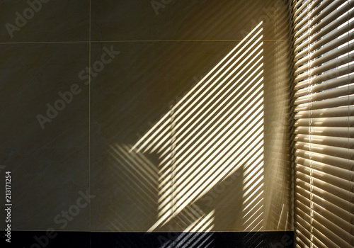 Shadow and light through blinds window on tiled wall. Abstract form morning light and shadow on the wall.