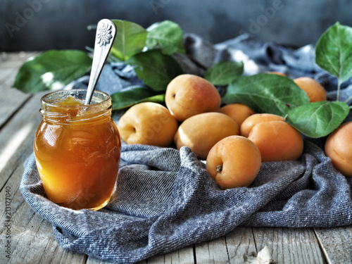 Fresh apricots and apricot jam in jar and green leaves on rustic wooden table.