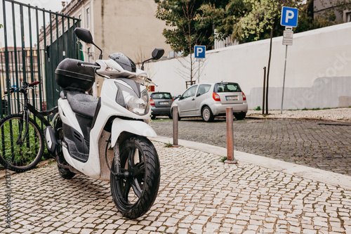 Parking on the street in Lisbon in Portugal. A motorcycle, a car and a bicycle are parked on the street. In the foreground is a motorcycle. Rainy weather