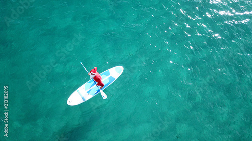 Photography Aerial drone of Santa Claus paddle surfing in Caribbean turquoise clear waters