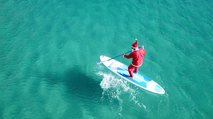 Aerial drone of Santa Claus paddle surfing in Australian emerald clear sea waters