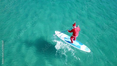 Aerial drone of Santa Claus paddle surfing in Australian emerald clear sea waters