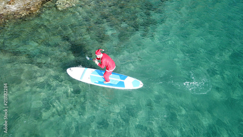 Photography Aerial drone of Santa Claus paddle surfing in Caribbean turquoise clear waters