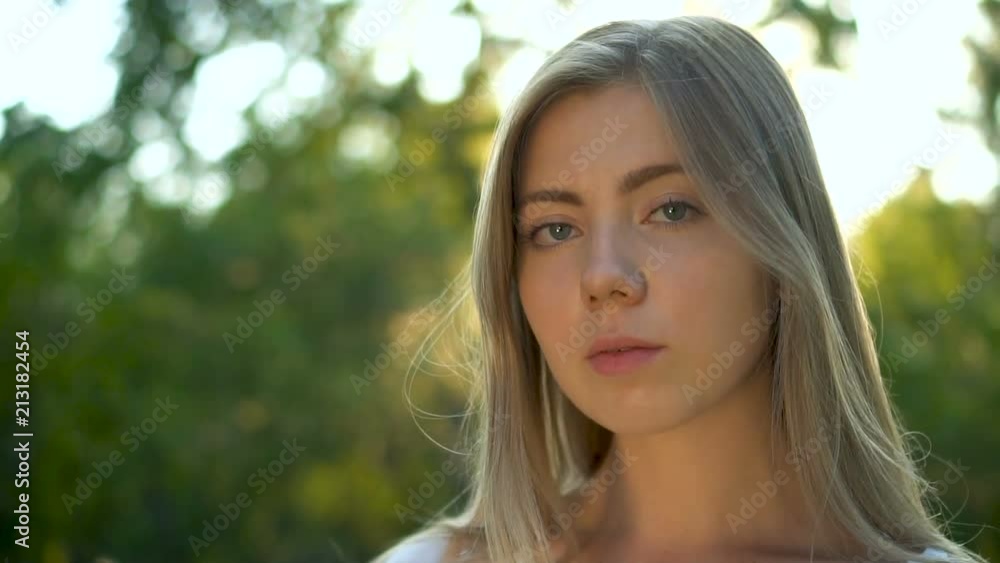 Beautiful blonde young woman in the summer garden looking at camera at sunset. Close up slow motion sunshine lens flare Beautiful blonde young woman in the summer garden looking at camera at sunset. Close up slow motion sunshine lens flare