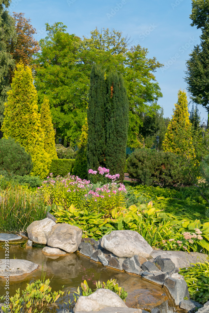 A small lake with decorative stone boulders, small flowers and coniferous trees A small lake with decorative stone boulders, small flowers and coniferous trees