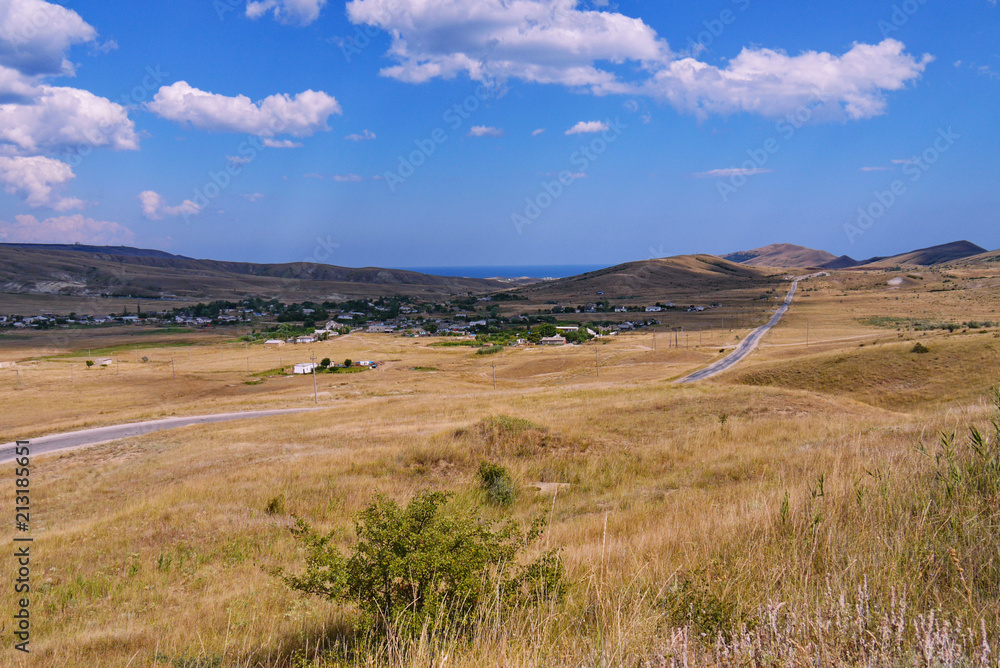 a long empty road, passing through a dry valley covered with grass among the mountains against a blue cloudy sky. place of rest, tourism, picnic