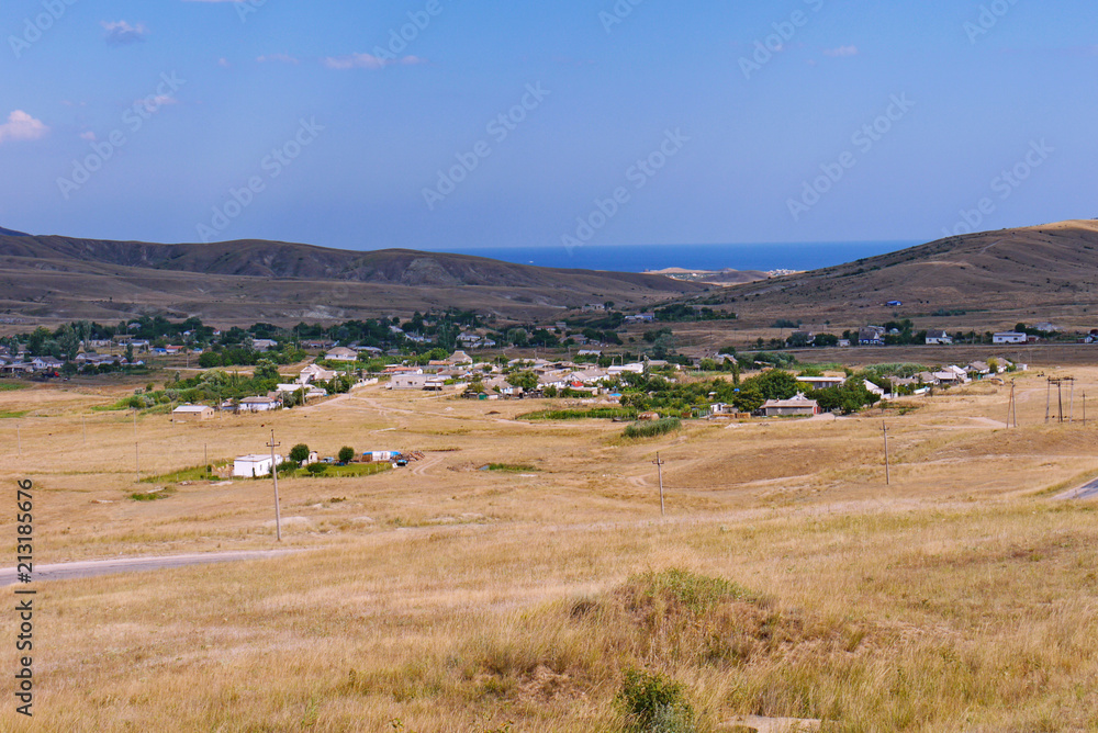 the town spread out in a valley covered with dry yellow grass, on which the road runs along the background of the hills