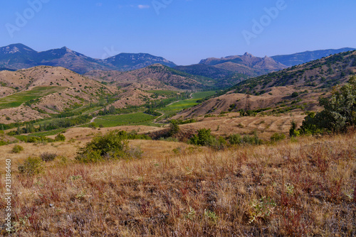 mountain landscape with a burning sun on the hills of grass and greens in the valley  against the background of the blue sky