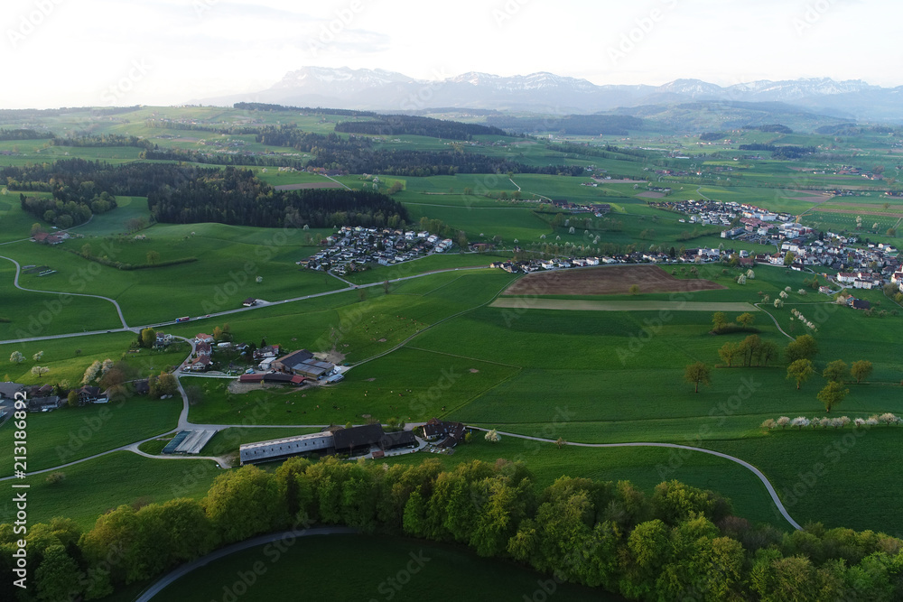 Swiss lowland with villages, farms and the Alps in the background on a spring morning