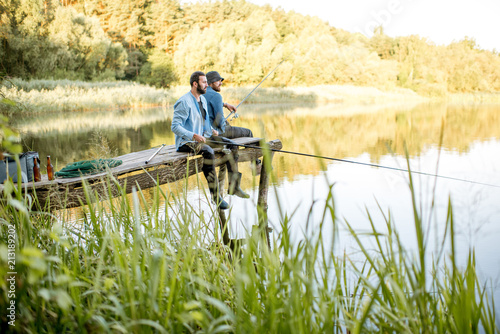 Dwaj męscy przyjaciele ubrani w niebieskie koszule łowią razem z siatką i wędką siedzącą na drewnianym molo podczas porannego światła na jeziorze