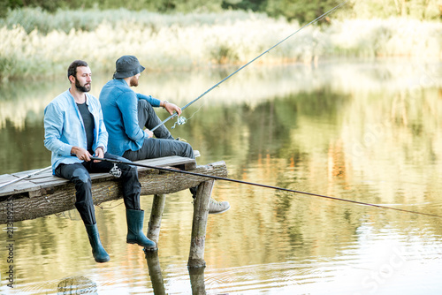 Print op canvas Two male friends dressed in blue shirts fishing together with net and rod sittin