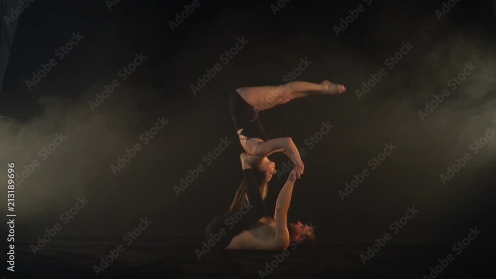 A woman jumps on the feet of a man and does a somersault, acro yoga in the smoke