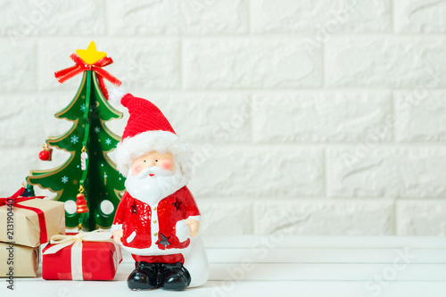 Art of Christmas ,happy new year gift red box presents with Santa Claus model toy and Christmas tree decoration on white wooden table background with copy space. Holiday and festival idea concept.