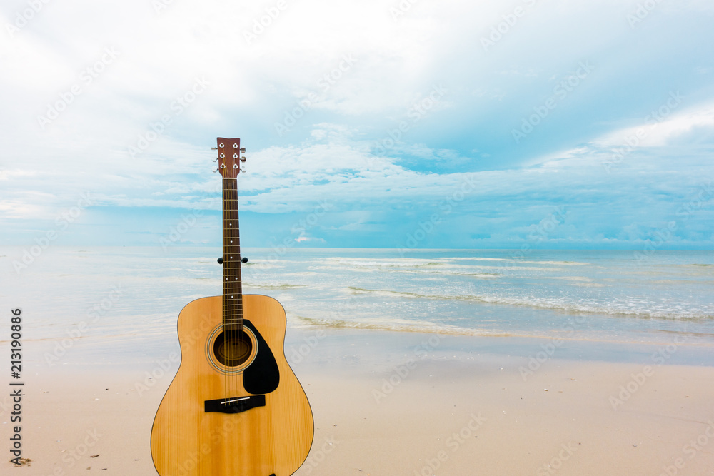 Fototapeta Acoustic guitar standing at tropical beach with blue sky background.