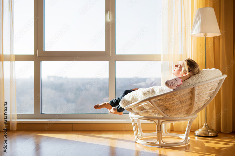 Woman relaxing in chair by the window - obrazy, fototapety, plakaty 