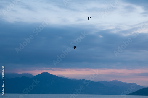 Sunrise on the lake. Panorama of the early morning. mountain in silhouettes and the rays of the rising sun. Birds flying in the sky. Sunrise on Lake Garda  Italy