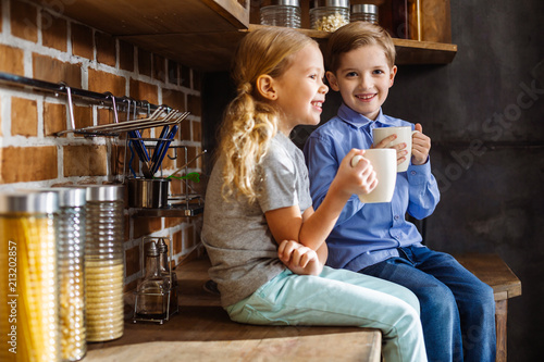 Positive little siblings drinking tea in the kitchen photo