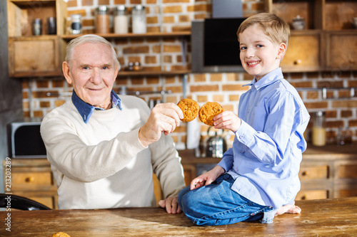 Positive little boy eating cookies with his grandfather