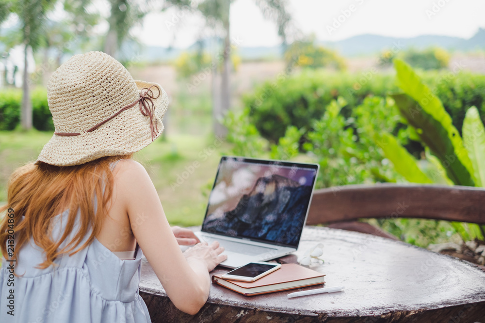 Fototapeta premium Young cute brown hair woman wearing cream hat using laptop notebook for education and writing text in a natural park, Technology social media concept.