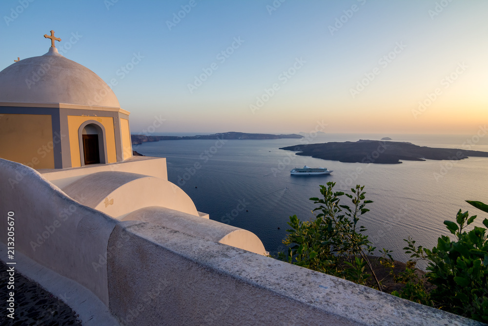 Elevated romantic sunset scene on Santorini. Fira, Greece, from above. Amazing golden hour view from public path walk towards volcano in the caldera. Shortly before the sunset, church in the image