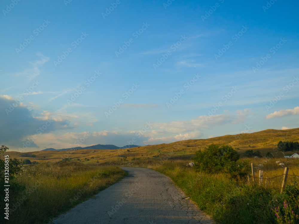 Movement on the road in the countryside in the evening with yellow meadows on the sides and pretty village houses Movement on the road in the countryside in the evening with yellow meadows on the sides and pretty village houses