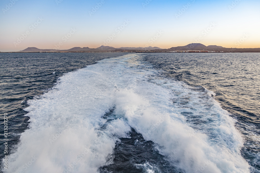 Obraz premium spume of ferry ship with lanzarote skyline in background
