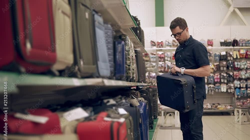 Man trying to fing new suitcase for a trip. Man preparing for vacation. Shopping for a new bag. Nice, big luggage. Checks on the handle. Man trying to fing new suitcase for a trip. Man preparing for vacation. Shopping for a new bag. Nice, big luggage. Checks on the handle.
