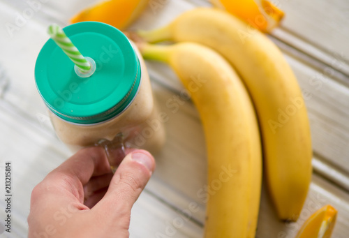 Glass jar with banana and orange smoothie in hand
