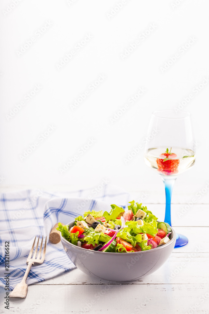 Fresh greek salad served in bowl with glass of white wine.