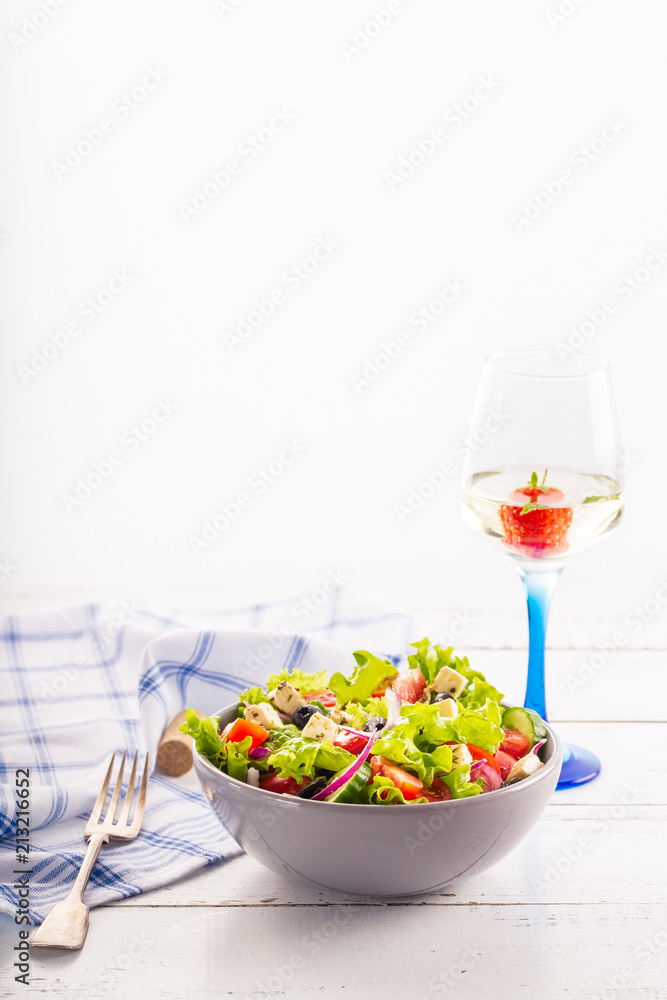 Fresh greek salad served in bowl with glass of white wine. Fresh greek salad served in bowl with glass of white wine.