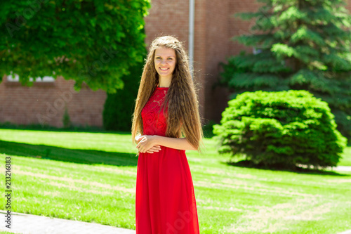 Cute young woman in long red dress walk in park