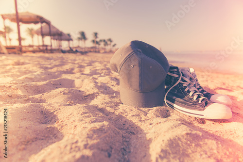 sneakers and cap on sand sunset beach with sea line on horizon photo