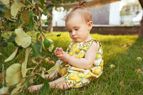 The happy young baby girl during picking apples in a garden outdoors