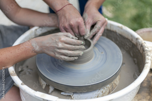 pottery training, a close-up of a man potter teaches a woman how to properly mold a bowl of brown clay on a potter